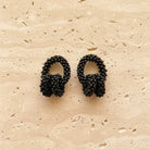 Pair of black beaded earrings on a beige stone surface