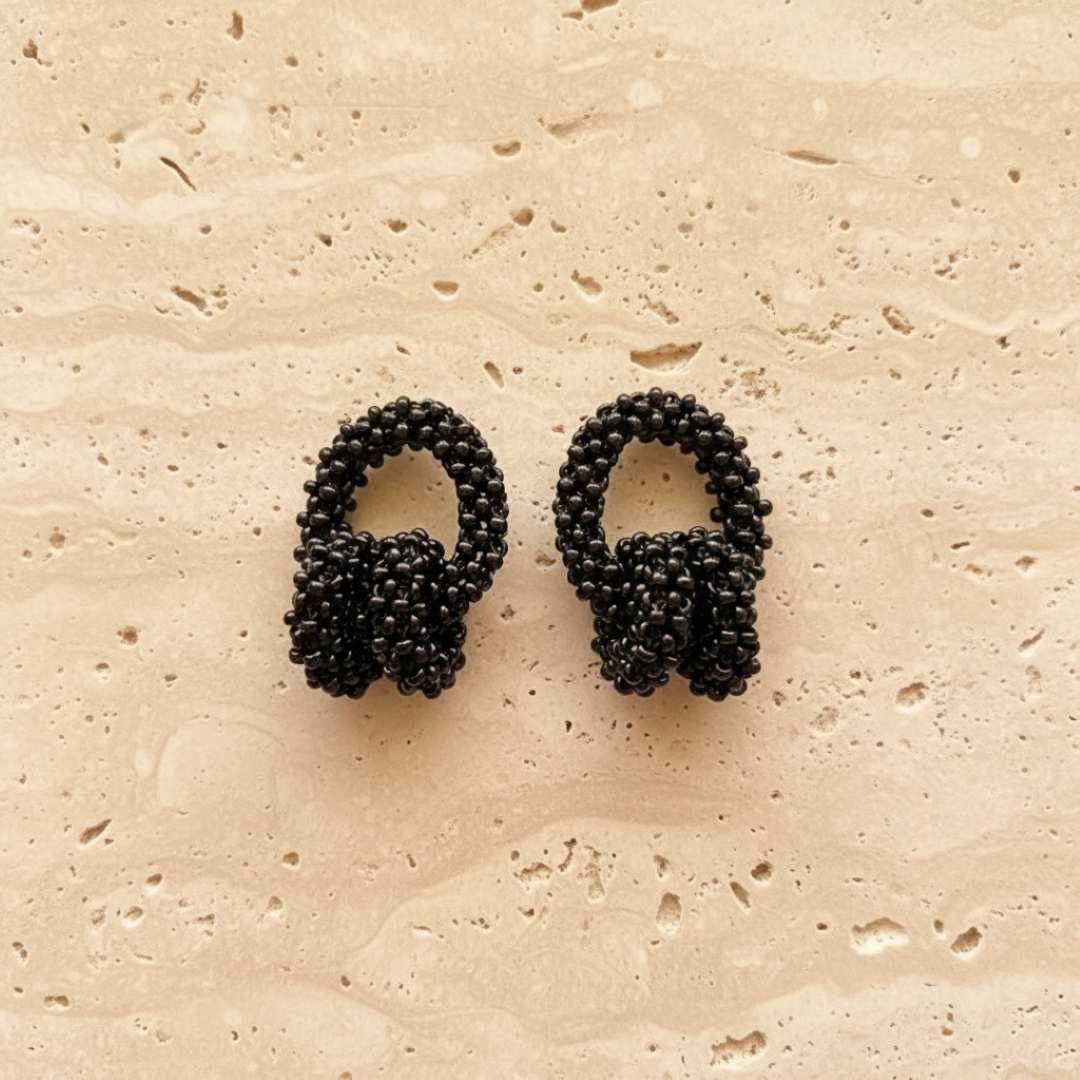 Pair of black beaded earrings on a beige stone surface